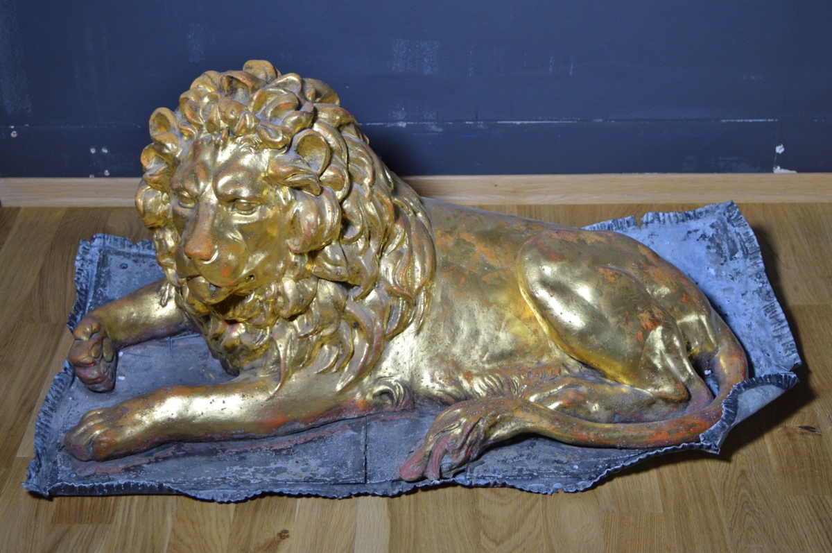 Løve-figur dekket med bladgull, liggende på en plate.