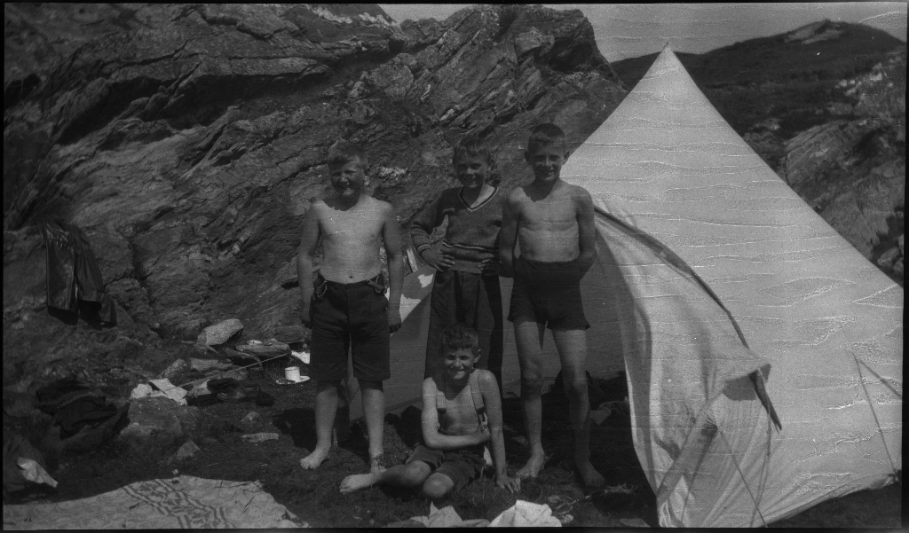 Barn og unge på og rundt stranda i Vigdelsvika. De fleste har satt opp telt, noen soler seg og noen bader. Den ene gutten på bilde nr. 6 holder et flytebelte.