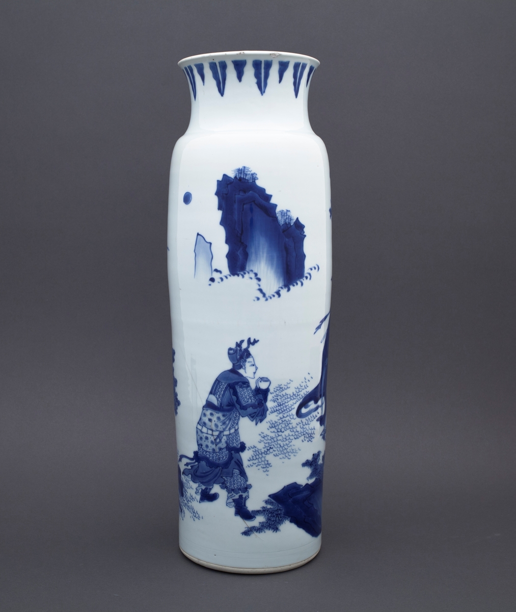 Tre mennesker står foran et stort tre. I bakgrunnen ser vi to fjelltopper. En mann står med foldete hender foran en annen mannsfigur. Han har skjegg, et sverd på ryggen og han holder i en vifte. Ved siden av mannsfiguren med sverd og vifte finner vi en kvinneskikkelse, som også holder i en vifte.