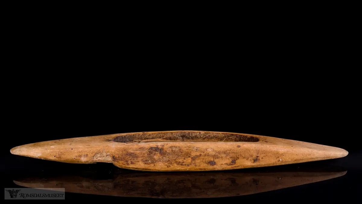 Avlang, båtformet med ovalt hull midt på kroppen. Festehull for spoler og spor for utføring av tråd.