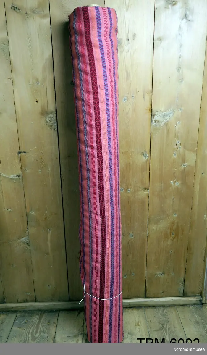 Rull med møbelstoff. Stripete, ein slags husflidsmønster. Hovudfarge rosa. Kanskje produsert for hyttemøblar.