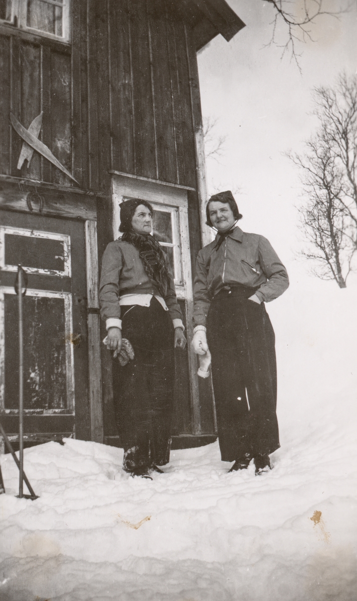 To kvinner utenfor en bygning. Over døra er det spikret opp to skitupper.