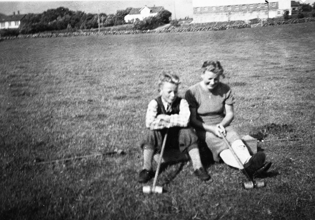 Odd Time (1.6.1926 - 9.8.1981) og Ingrid Maria Time  g. Oma (24.11.1920 - 17.6.2014) med krokketkøller på kjelva. Garden - Time bnr. 2 - i bakgrunnen.