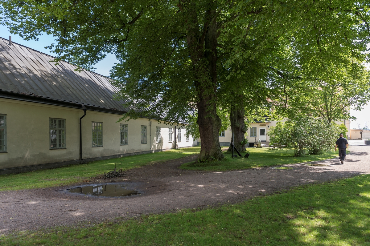 Fotodokumentation av byggnader på Marinbasen i Karlskrona. Till vänster i bild. Pjäsverkstaden. Ursprungsanvändning som verkstad för kanoner eller artilleripjäser. De äldsta delarna i byggnaden uppfördes under 1730-talet då de östra och västra längorna byggdes.