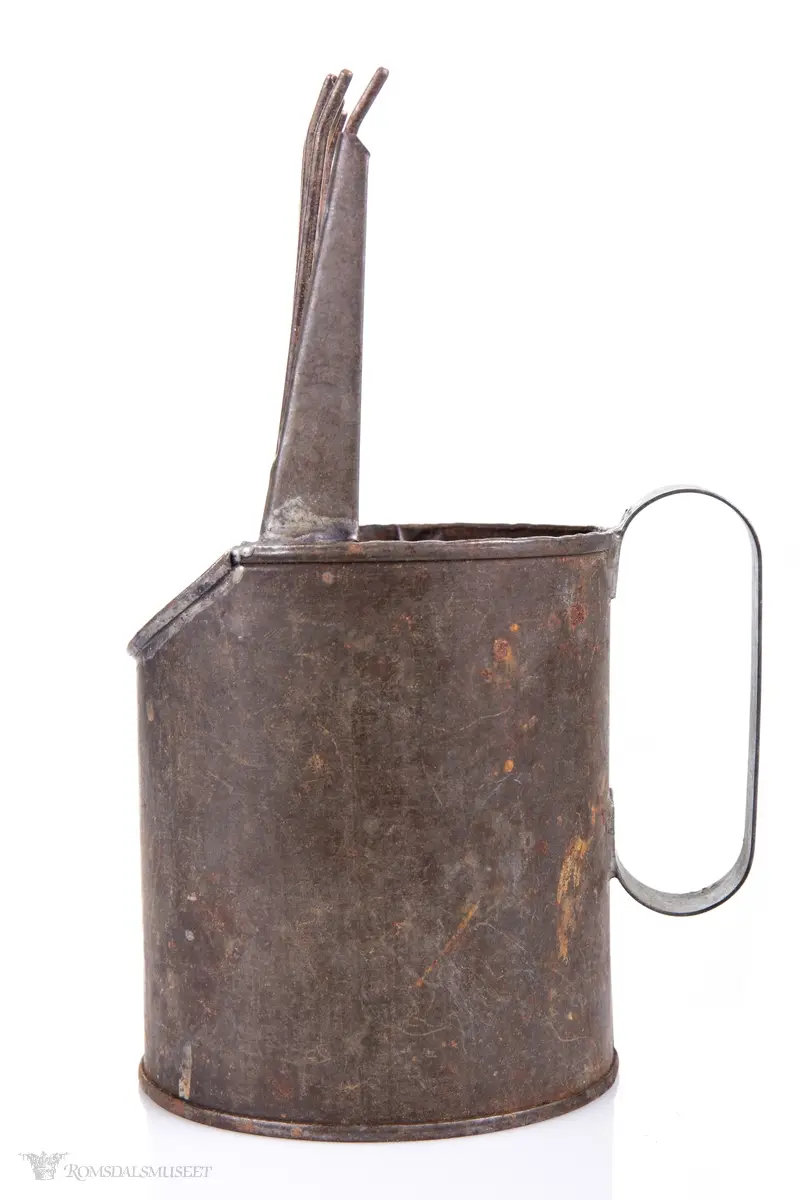 Sylinderformet blikkboks som kropp, med påloddet buehåndtak og en skråstilt plate med tenner foran.