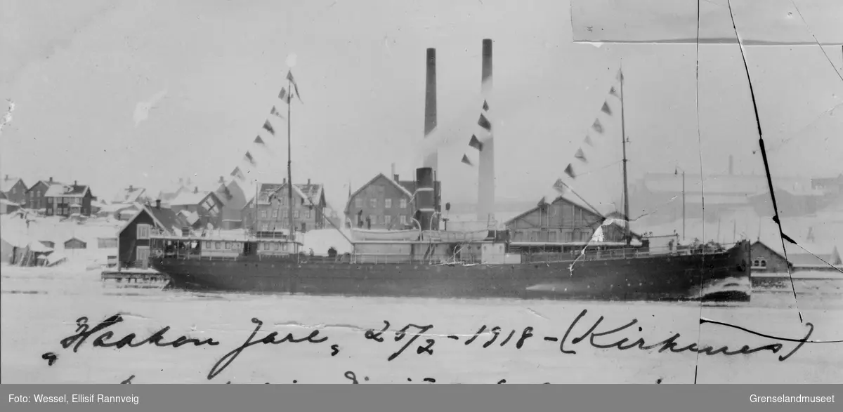 Dampbåten "Haakon Jarl" ligger til kai i Kirkenes. Direktør Wiulls avreise 25/2-1918. Til høyre kullageret til damskipsselskapet. Til venstre dampskipsekspedisjonen. Ellers ser vi post, telegraf og toll.