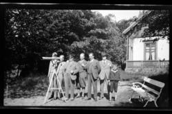 Seks menn og en gutt ved en kikkert plassert i hagen til fam