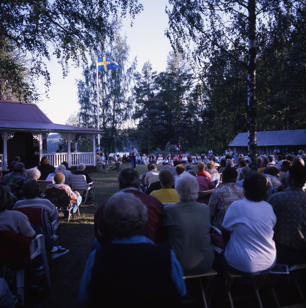 "Törnkvällen" 14 juli 1997. Festkväll med uppträdanden, musik och sång vid Albert Vikstens torp vid Ängratörn. Mycket publik har samlats och de sitter i medhavda stolar i kvällsssolen.
