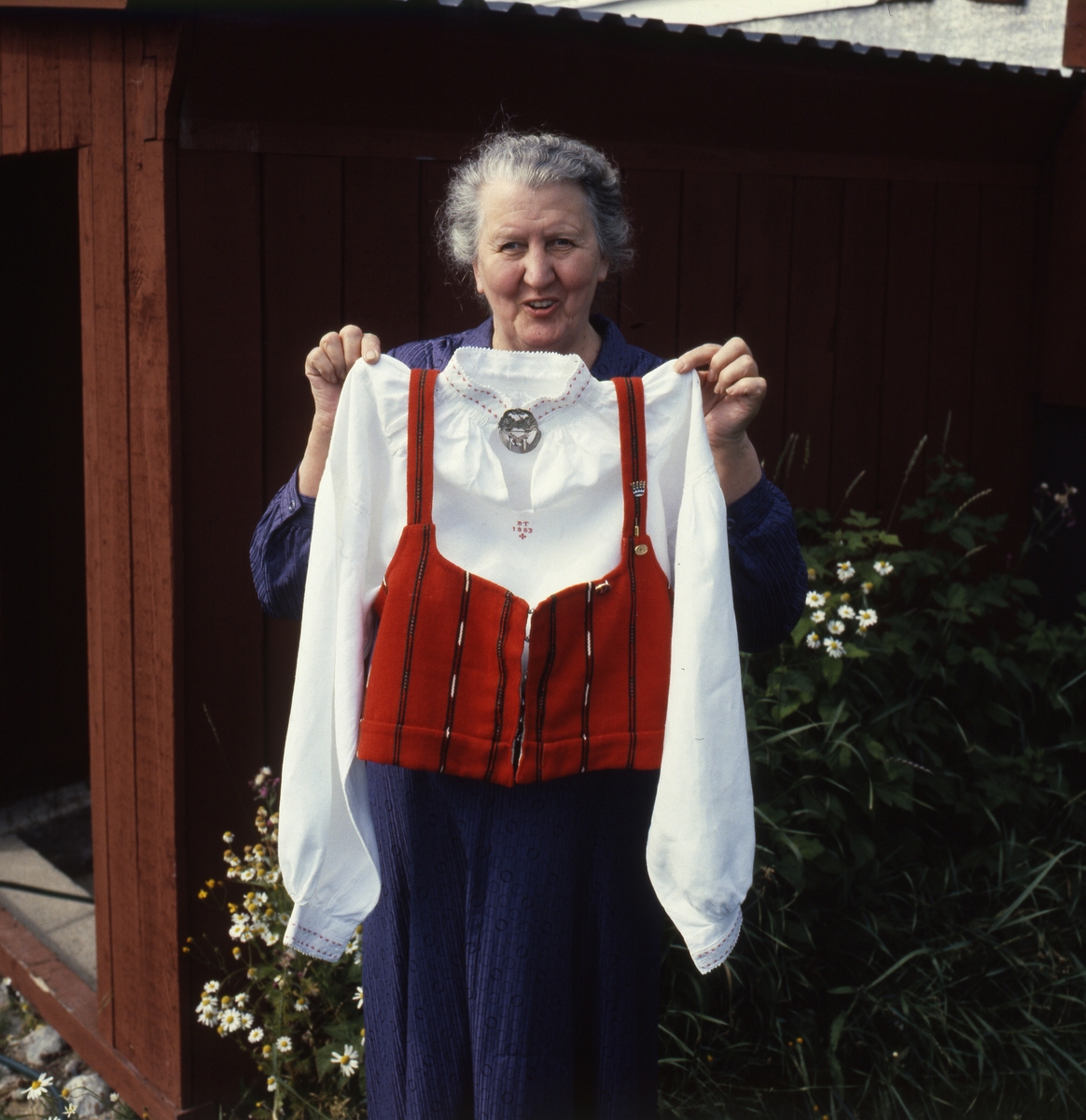 En kvinna håller upp en folkdräkt med liv, skjorta och kjol samt tillhörande smycken.