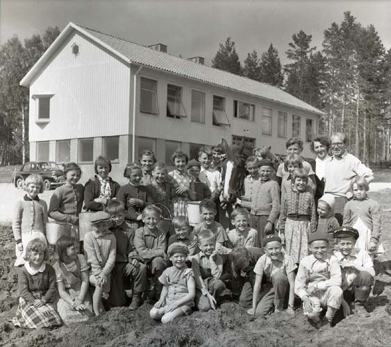 Gruppbild av barn och vuxna framför en skolbyggnad i Annefors. Unga Odlare, klubbodlingar, potatissättning i Annefors 31 maj 1954.