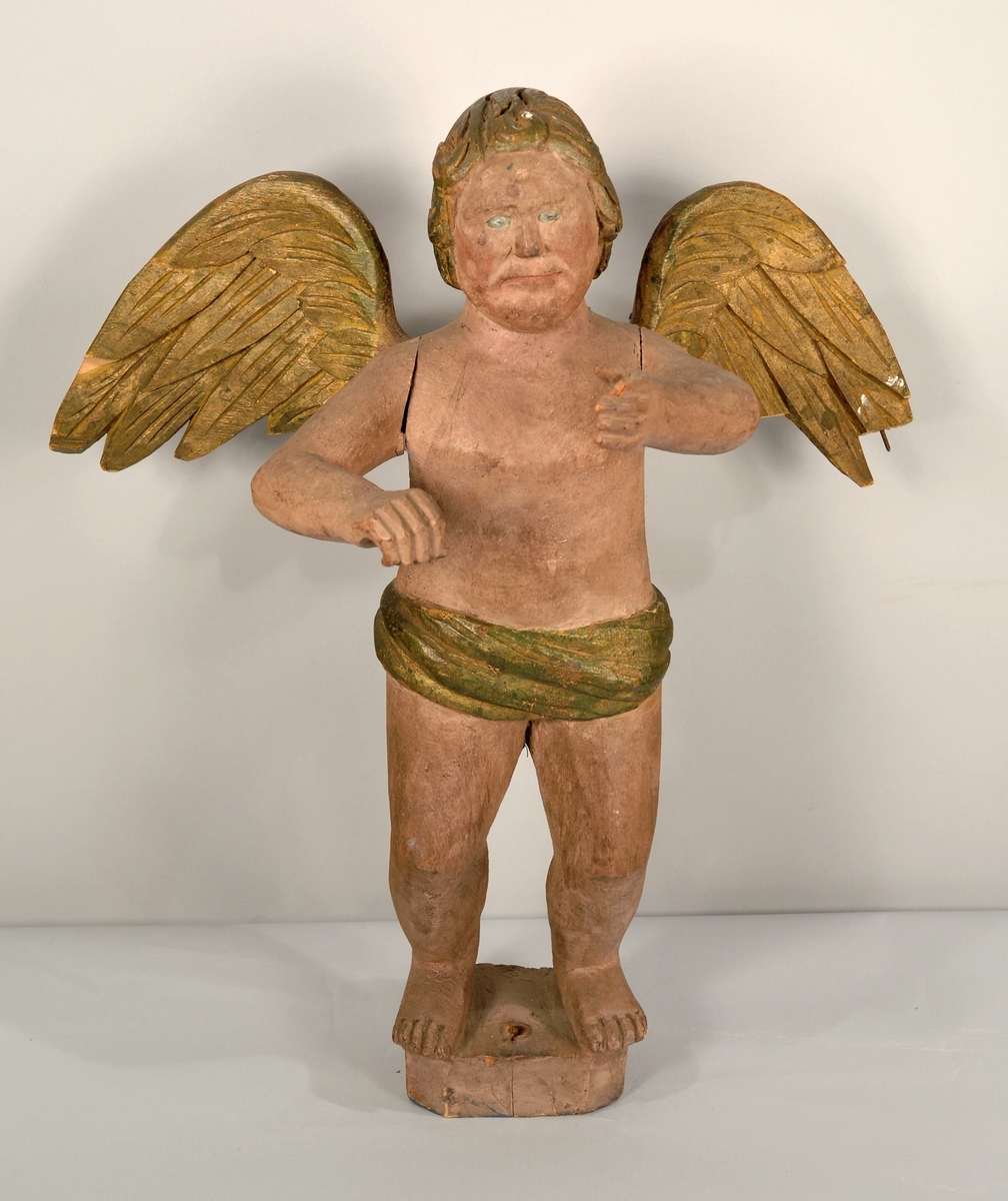 Trefigur, engel med forfylte vinger, hår og lendeklede som er drapert. Står på en trekloss. Engelen har fremstrakte armer.
