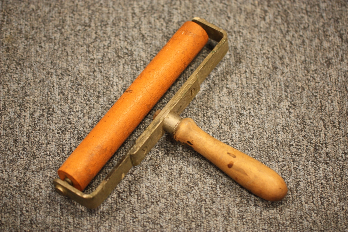 Gummirulle montert i ein stålklave med eitt handtak midt på.