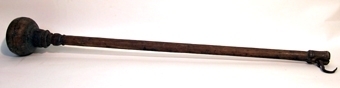 Besman av trä med krok av järn samt skåror och stift som används som skalor. I botten sitter en runt, svarvat klot.