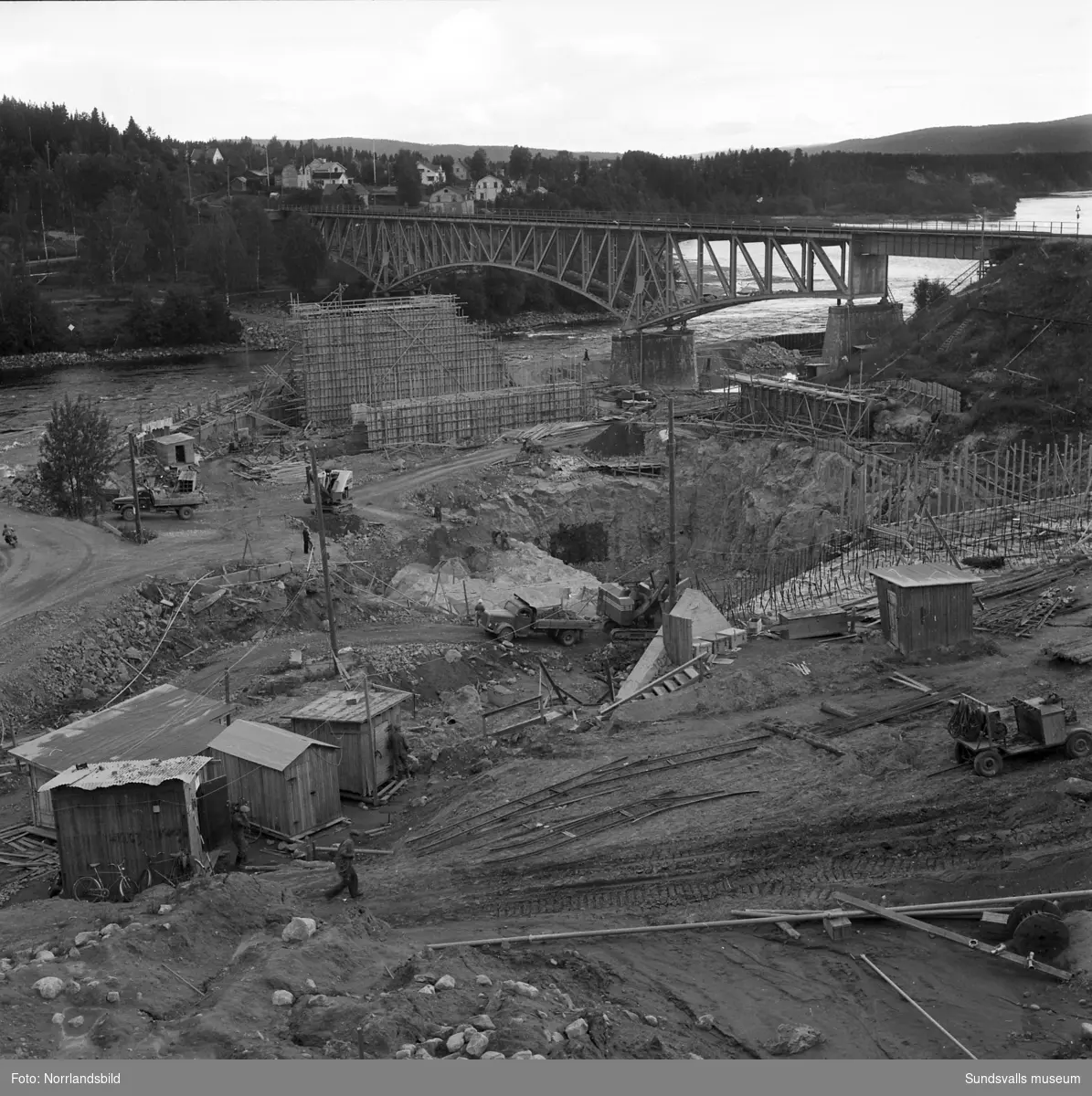Kraftverksbygget i Bergeforsen framskrider. Vyer, bergsprängare, svetsare och administrativ personal. På första bilden syns den gamla landsvägsbron till vänster samt järnvägsbron i högerkanten av bilden.