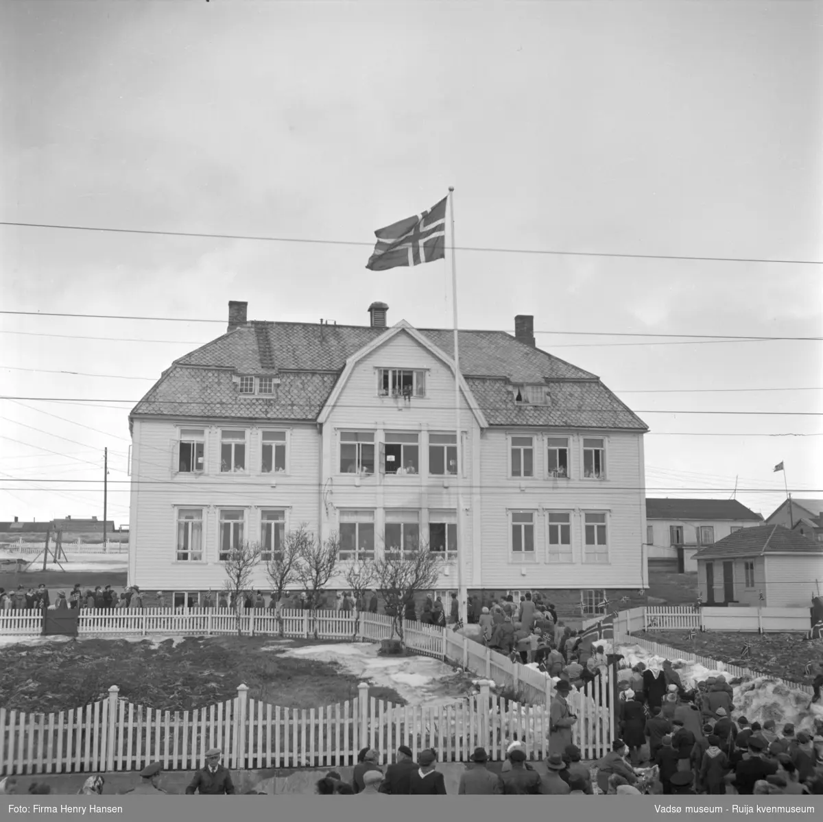 Vadsø 17 mai 1952. Barnetoget har tradisjonen tro stoppet opp foran Kysthospitalet i Oscarsgate som da fungerte som byens sykehus.  Snødunger ligger ennå.