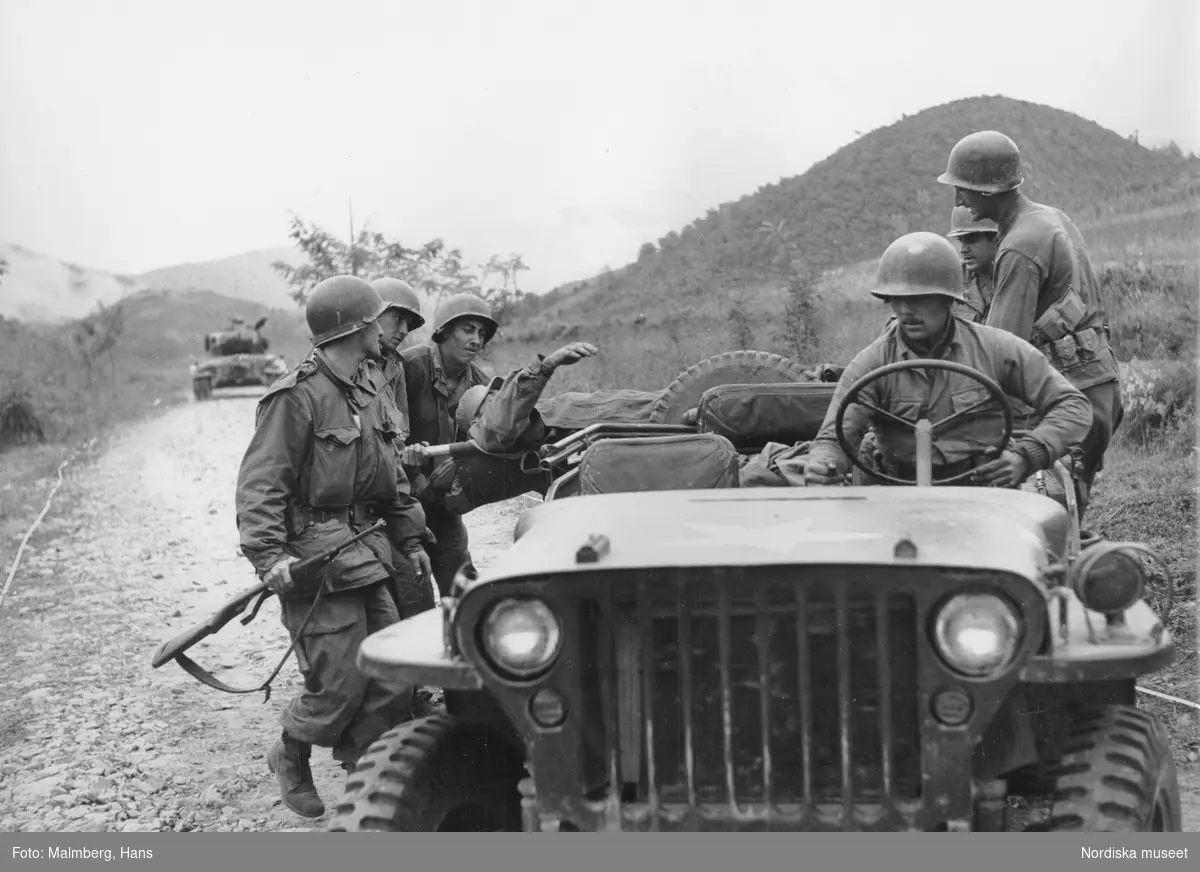 Koreakriget. En sårad amerikansk soldat på en bår lastas på en jeep av sina kamrater.