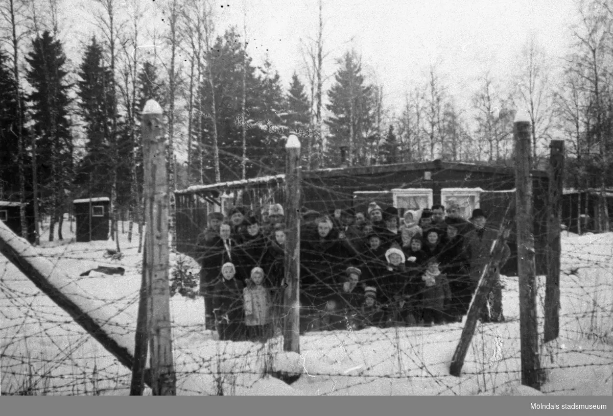 Estländska flyktingar i karantänläger hösten 1944. Familjerna står bakom en taggtråd som omringar det så kallade karantänlägret i Byringe, Örnsköldsvik. I lägren avlusades flyktingarna och de läkarundersöktes grundligt. Deras kläder och tillhörigheter brändes. Vid minsta sårbildning eller spricka i huden fördes flyktingarna till sjukhus. Rädslan för smittsamma sjukdomar var stor under rådande krig. Hösten 1944 flydde 32.000 estländare från kriget i Estland till Sverige. Ett sextiotal personer tog jobb på August Werners textilfabrik i Lindome. 
Kvinnorna arbetade i spinneriet och männen i färgeriet. 
Mer information finns i uppsatsen "Estländska textilarbetare i Lindome" som finns i Mölndals stadsmuseums interna arkiv.