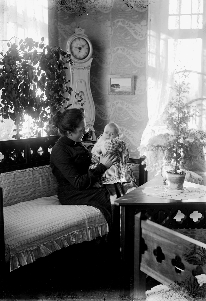 Rumsinteriör, en kvinna med ett litet barn i soffan.
Sigrid Thermaenius (född Grenander) med sonen Olle, född 1902-08-30.
Bilder från samma fototillfälle: OLM-92.149.128-1 och OLM-92.149.157-1