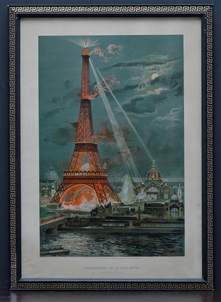 Et fargetrykk der motivet er  Eiffeltårnet som lyser opp over Paris. Eiffeltårnet er farget rødt mens det sender ut to klare lysstråler. I forgrunnen kan man se Seinen med en elvebåt som kommer inn fra venstre. Plakaten er fra Verdensutstillingen i Paris (06.05-31.10.1889) der utstillingens største byggverk og symbol var nettopp Eiffeltårnet. Buen til tårnet utgjorde porten til utstillingen. Rammen er en treramme som er malt svart og som har enkel profilering innerst. På rammen er det også en en firkantbord som er malt i gull. På baksiden er det festet en papplate med metallstifter. Opphenget er to runde metallkroker som er festet på hver sin side i rammen.