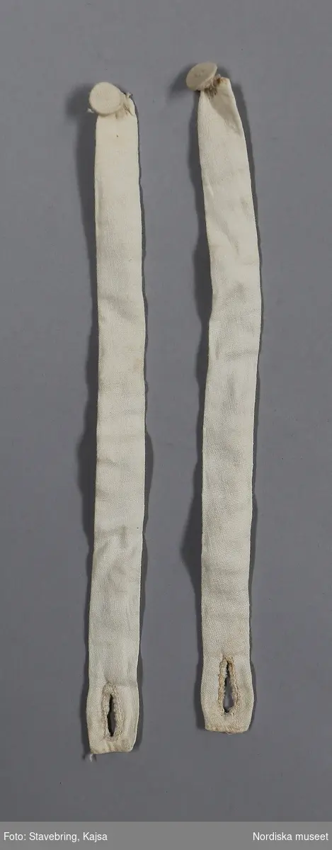 Katalogkort finns.

Bruddräkt bestående av a. kjol, b:1-2. tröja. c. band. Från Blomhemmet under Altorp.

Kjol och tröja av vit tunntrådig tätvävd bomullslärft
b:1. Tröja, kort med skört i sen 1700-talsmodell. 
2 framstycken/sidstycken  och 2 ryggstycken kraftigt avsmalnande ned mot skörtet bestående av 4 veck som hålls samman med några stygn Som dekor vid skörtet två sammanhängansde tofsar av vitt bomullsgarn, gjorda som en "smällkaramell" som lindats på mitten med utstående trådar åt sidorna som bildar tofsarna. Infällda skörtkilar i sidorna. Smal fåll i nederkanten med en rad efterstygn. Isydd ärm med skarvkilar under armen, på axeln 9 lagda veck, rak ärmkant. Vid halsringning, knäppning saknas. Helfodrad med vit linnelärft ned till midjan, skörtet ofodrat. I midjan ripsband i linne smalrandigt i blått och rosa på vit botten, 8 mm brett, fastnäst med några stygn på 3 ställen. Knyts fram. Runt detta band är påknäppt 2 sydda band (b:2+) av bomullstyget, 1,5 cm breda försedda med en tygknapp och knapphål i ändarna.. Kan troligen ha knäppts fast runt ärmarna vid handleden.
/Berit Eldvik 2008-12-11