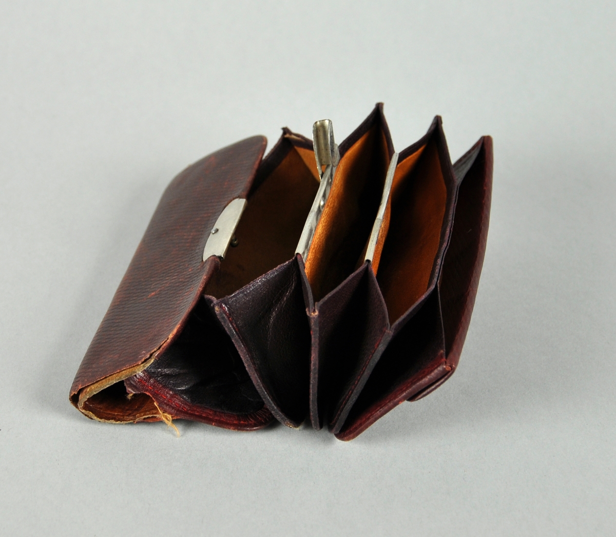 Lommebok av skinn, med lås i metall. Flere lommer kan trekkes ut. En av lommene har metallås.