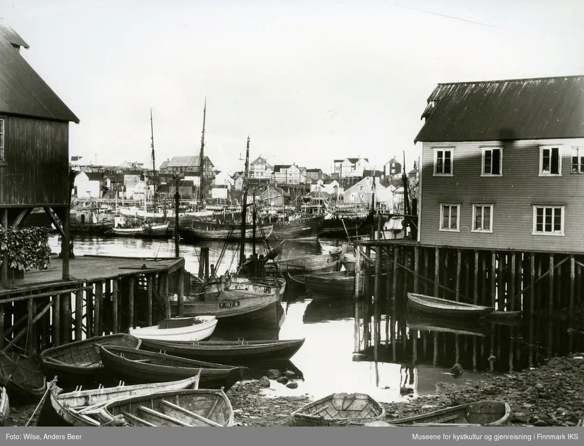 Honningsvåg (Finnmark). Indre havn med bebyggelse, fiskebåter og fiskehjeller. Båten i midten, med registrering F-107-K, er Må "Fuglen". Eieren i 1928 var J. Persen, Kåfjord. Må=motoråttring. 29. juni 1928. (Originalnegativet eies av Norsk Folkemuseum, W 32780)