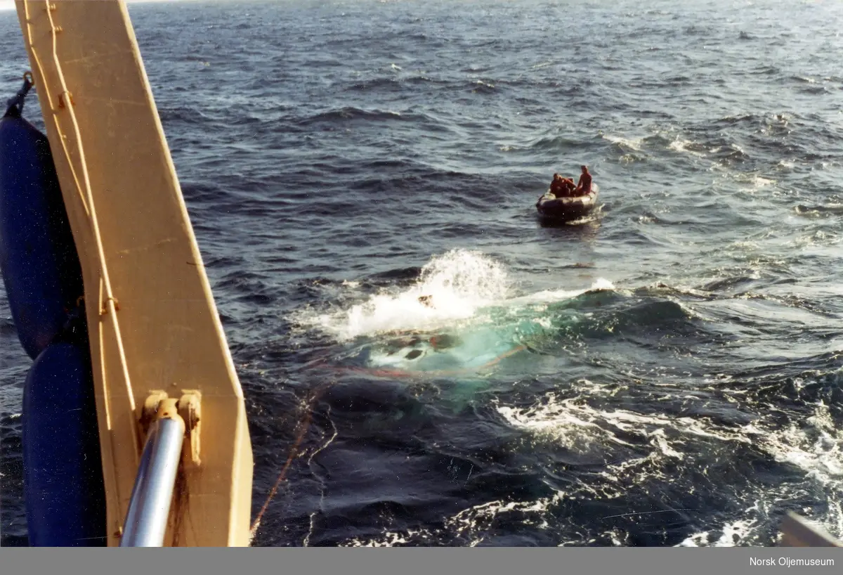 Den bemannede ubåten Oceanics er heist fra moderfartøyet Borgholm(?) og ut i sjøen der den er klar for dykk. så skumsprøyten står.  3 personer befinner seg i en gummibåt like ved siden.