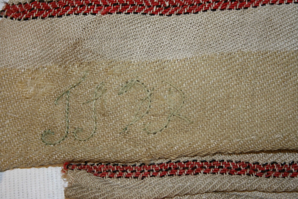 Teppe, sydd saman av 3 breidder, raud- og kvitstripet. Vove av ull og lin.