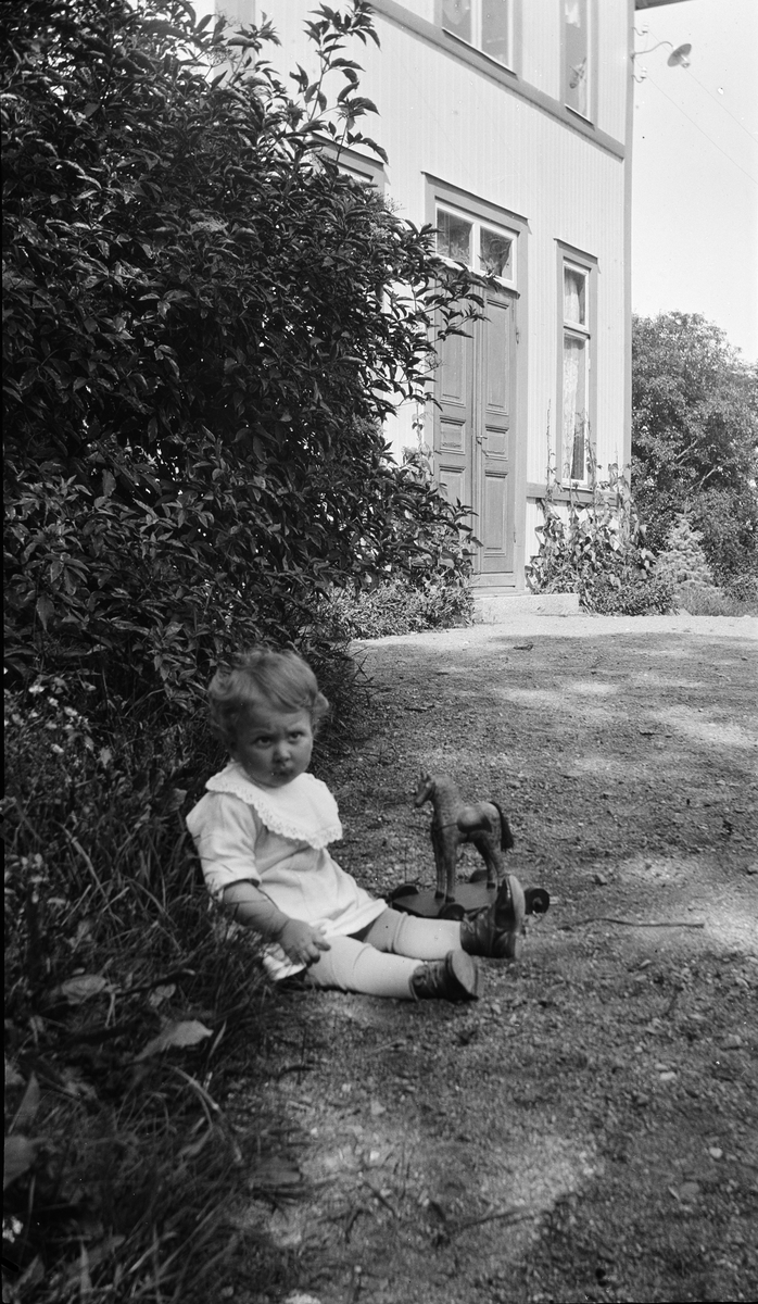 Litet barn sitter i trädgården, Uppland 1927