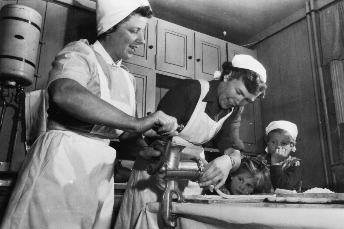 Pølsestapping på Stor-Gålås i 1956. Olaug Haugen sveiver kjøttkverna, May Platou passer på tarmen og døtrene Grete Platou og Marit Platou følger interessert med. Juleforberedelse.