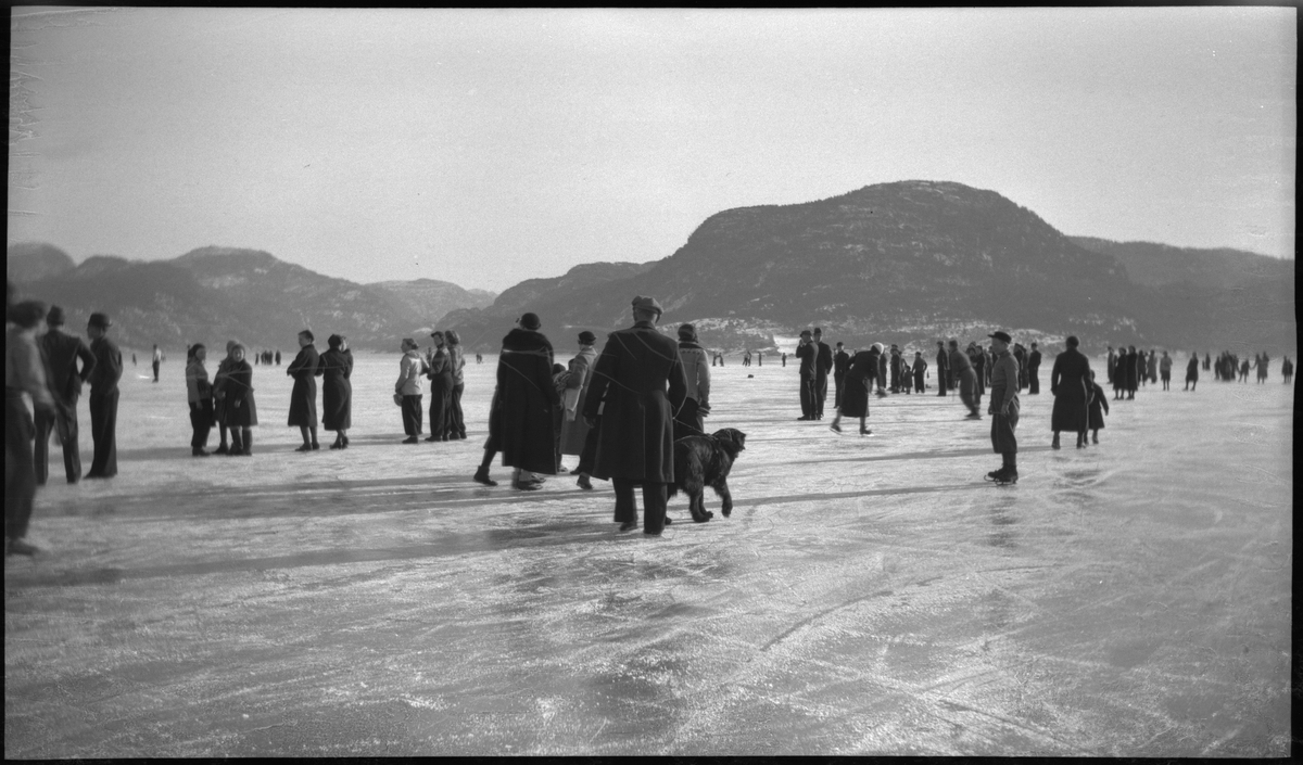 Bilder fra skøytetur ved Jørpeland. Det er mange folk på isen. De unge spiller bandy eller ishockey med hjemmelagde køller.