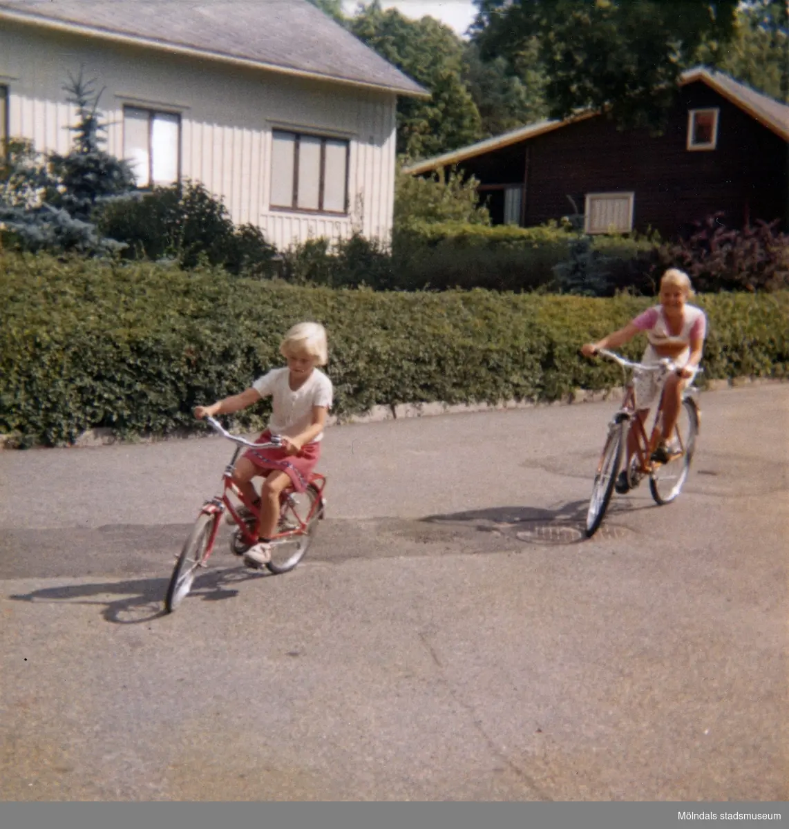 Systrarna Christine och Ingela cyklar på vändplanen i "Stusshålan" på Kryssgatan i Mölndal. På den här gatan lärde sig Christine att cykla. Ca 1976.