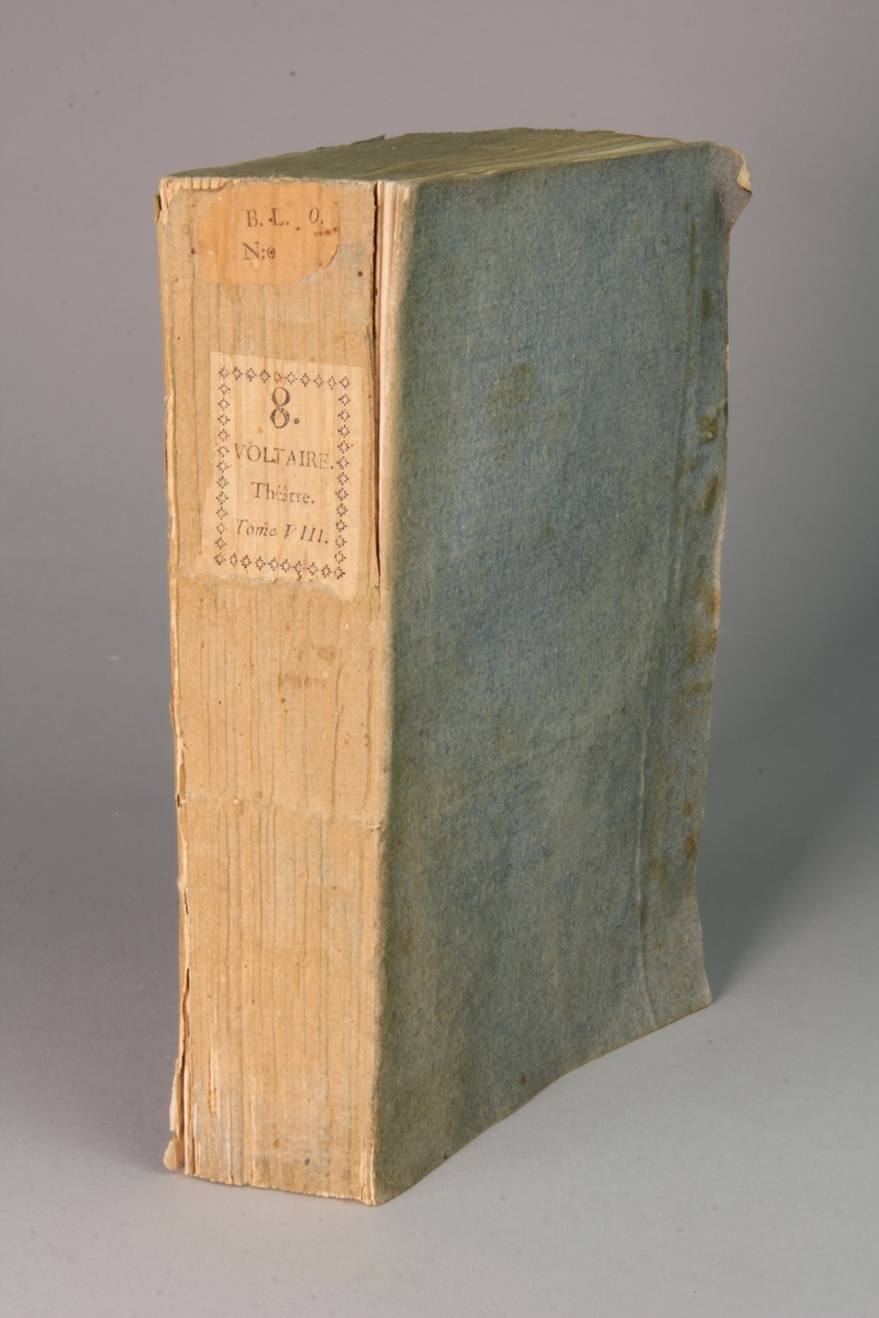 Bok, häftad,"Oeuvres complètes de Voltaire." del 8, tryckt 1785.
Pärm av gråblått papper, skurna snitt. På ryggen pappersetikett med tryckt text med volymens namn och nummer. Ryggen blekt.