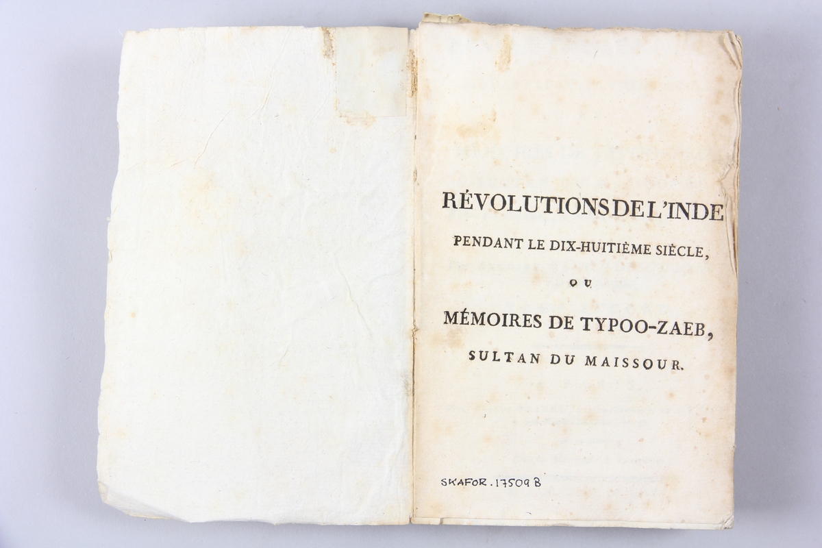 Bok, pappband, "Révolutions de l´Inde", del 2, tryckt 1796 i Paris. Pärmar av ljusbrunt papper, blekt rygg med tryckta etiketter med bokens titel och nummer, otydlig text. Skuret snitt.