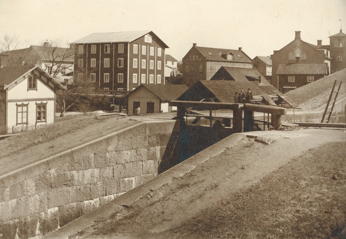 Motiv från Tannefors sluss i Linköping. I bakgrunden samlar sig kvarnbebyggelsen invid Stångåns fall. Tiden är omkring 1895.
