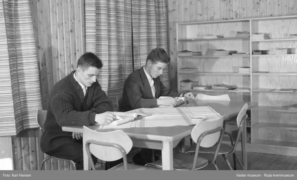 Finnmark Landbruksskole, Tana. 2 menn i lesesalen/biblioteket.
Skolen gikk først under navnet Fagskolen for Finnmarkens næringsliv.  I 1923 ble navnet endret til Finnmark landbruksskole. I førkrigsårene var det hektisk aktivitet ved skolen, det ble bl.a. reist et nytt internat i 1938. I august 1940 overtok tyskerne. All undervisning ved skolen ble innstillt og høsten 1944 ble bebyggelsen i Tana brent. Først i 1956 var gjenreisningen kommet så langt at det første kullet etter krigen kunne begynne. I 1958 ble arbeidet med det nye undervisningsbygget igangsatt. Inntil dette stod ferdig i 1960, måtte undervisningen foregå i internatbygningen. (www.nsd.uib.no)