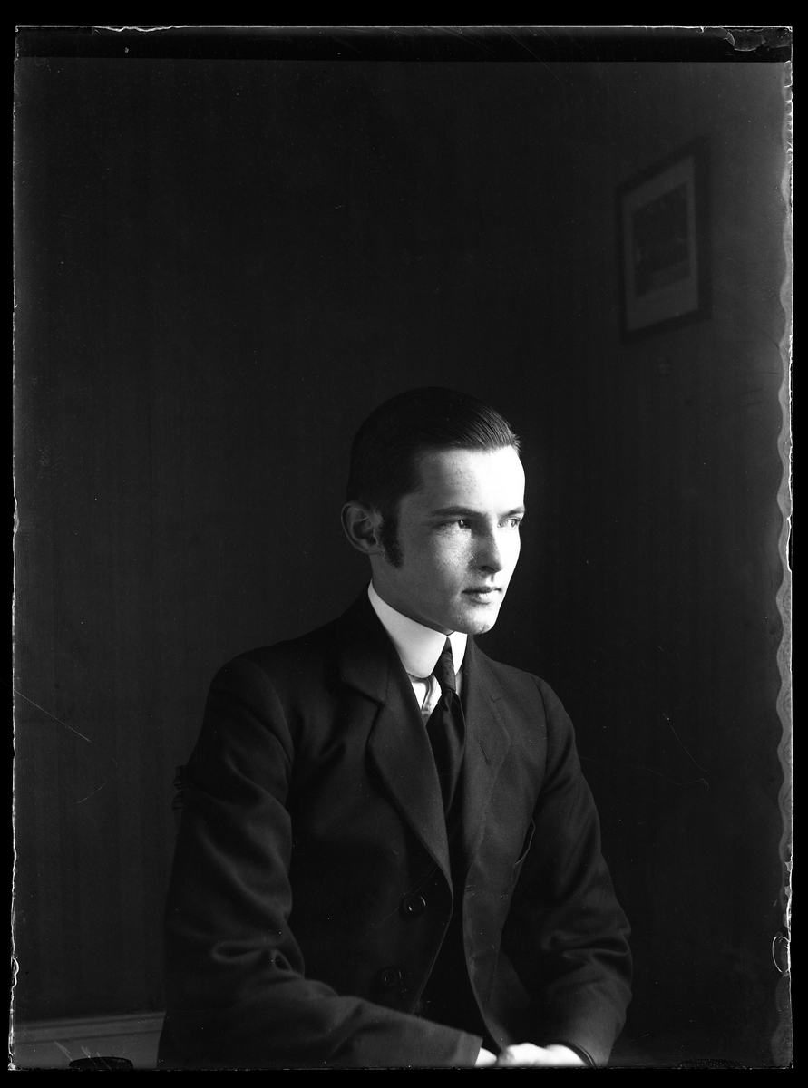 Porträtt av Folke Olsson i halvprofil, klädd i mörk kostym, skjorta och slips.