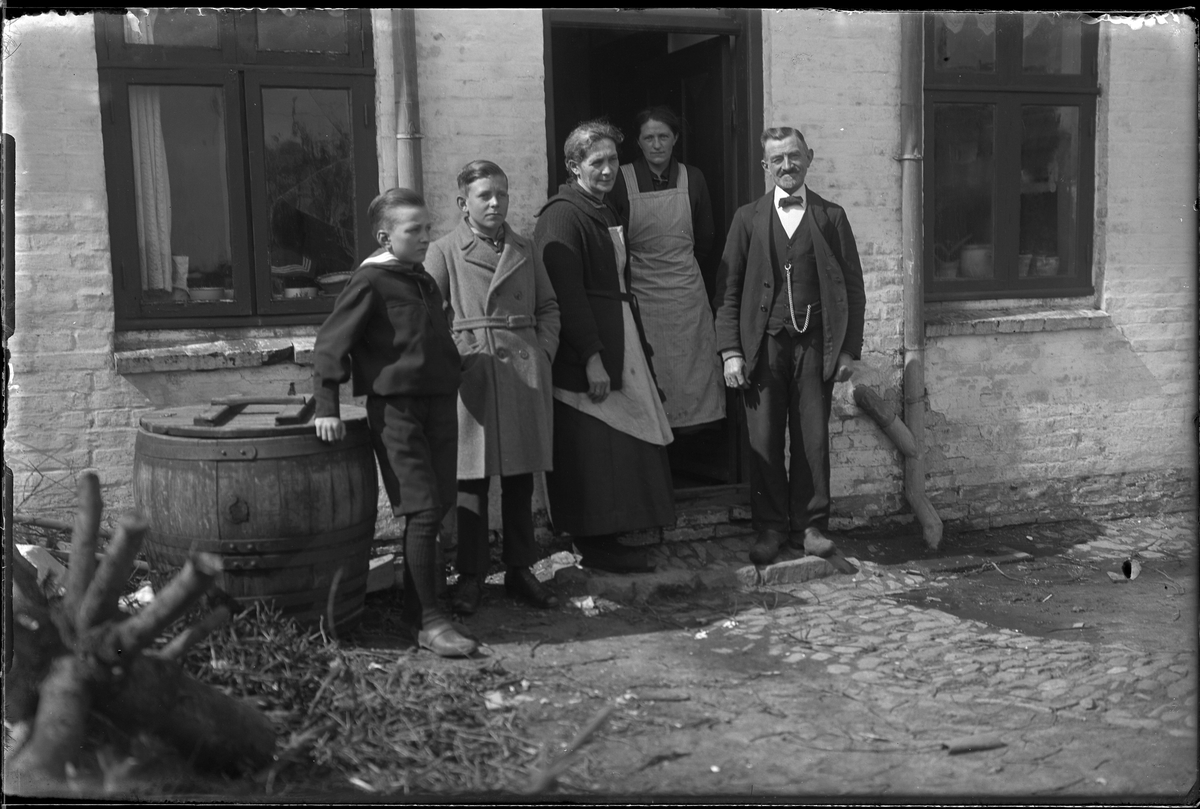 Två pojkar, två kvinnor och en man står i dörren till en vitkalkad tegelbyggnad. I fotografens egna anteckningar står: Danmarksresan, Petersén, Hjörring