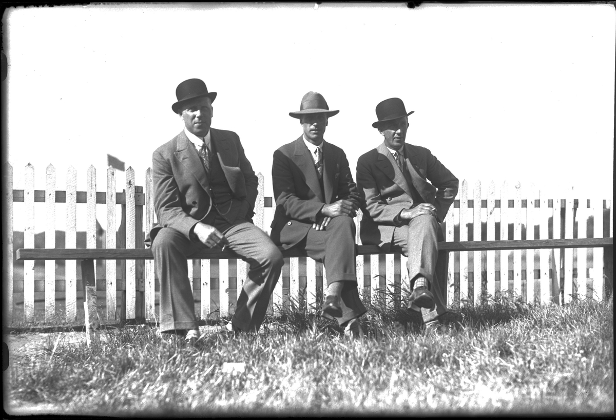 Tre män sitter på en bänk och röker. Fotot taget i samband med en fotbollsmatch. I fotografens egna anteckningar står det "Gunnar Johansson, Tell +1?"