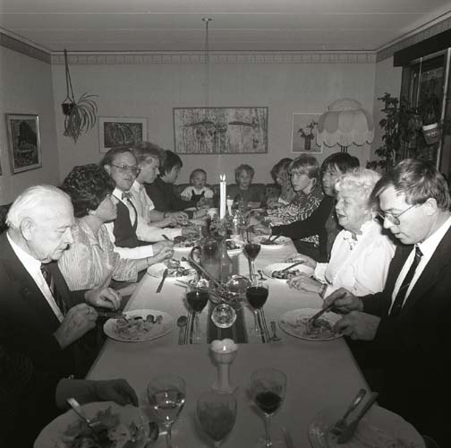 En grupp människor sitter församlade runt ett matbord och äter, 1985.
