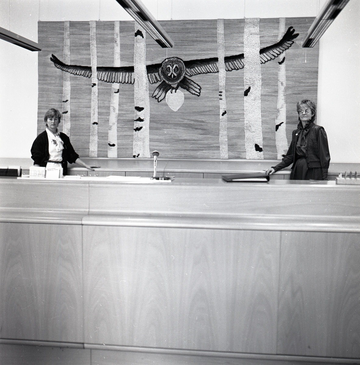 Två kvinnor står i en reception bakom vilken en tavla med Hildingmotiv hänger i Lidingö den 30 september 1985.