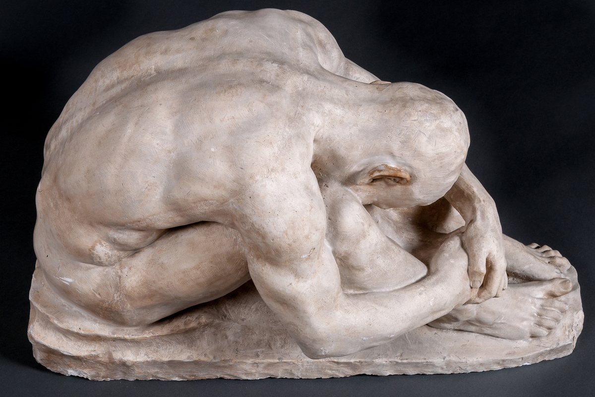 Skulptur i gips, detalj av gravmonument, kallad "Sorg", av John Runer. Återger en man naken sittande på marken, med huvudet ner mellan knäna.