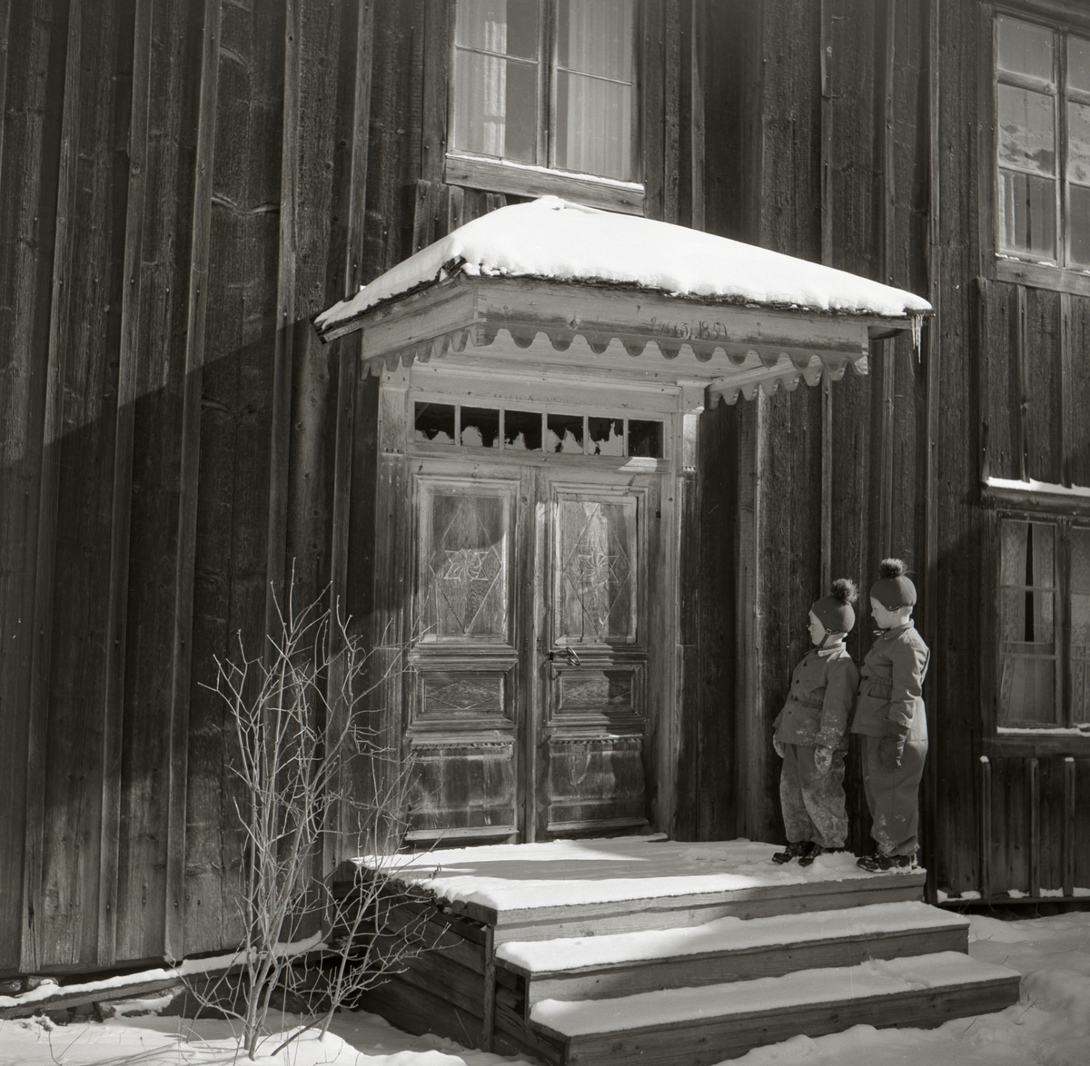 Två pojkar står under ett förtak vid hembygdsgården i Rengsjö,  byggnaden är Regnells östra.