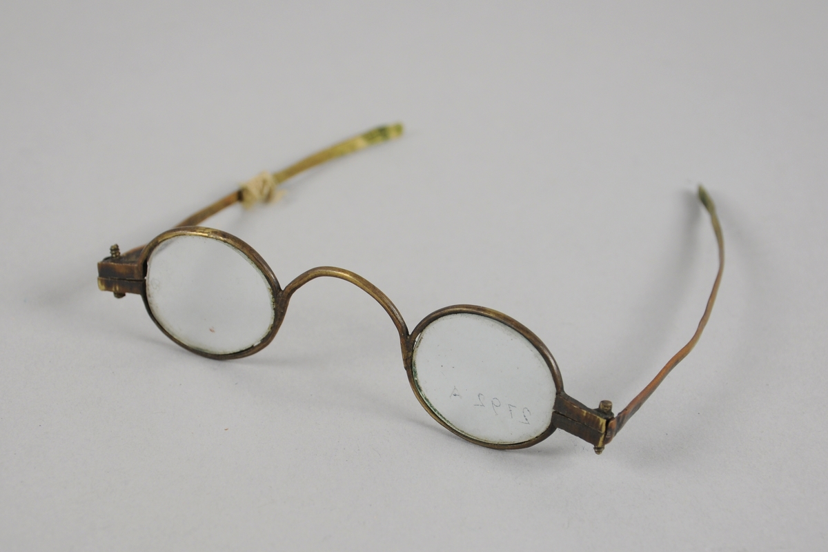Runde briller med metallinnfatning. Den ene brillestangen er knekt, og skjøtet med tråd.