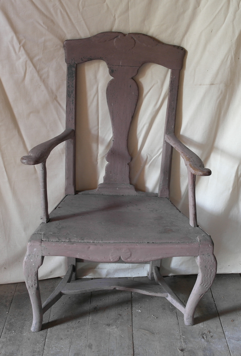 Stol i saget, skåret, høvlet, pusset og malt furu. Stolen er sammenføyd med trenagler. Den har et skåret toppstykke og svungne armlener. Ryggstolpene og bakbeina er i ett stykke, og det er bukkebein foran. Beina er skåret av. Underdelen har H-kryss. Stolen er opprinnelig malt grå og overmalt med lilla.