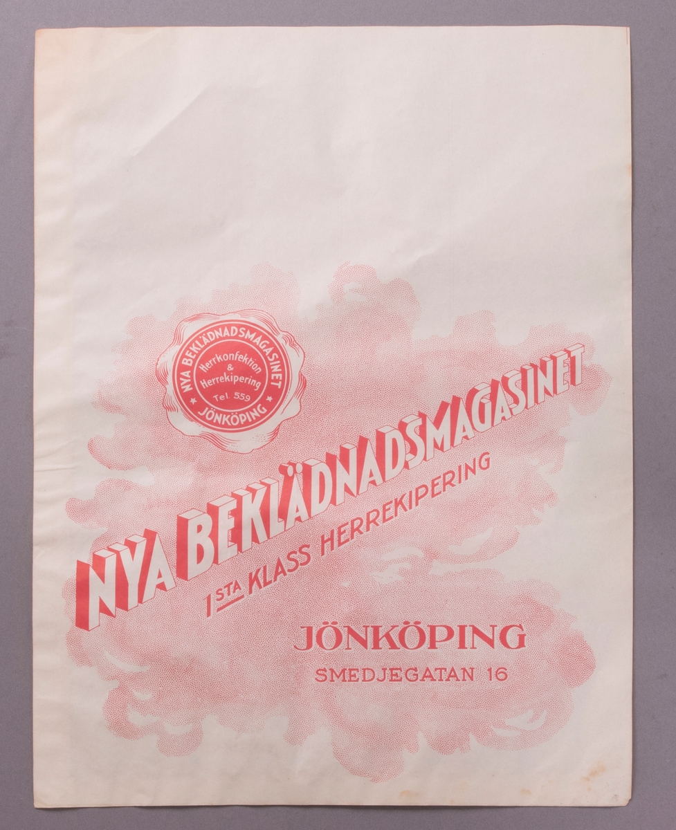 Påse av vitt papper med tryckta illustrationer och texter på båda sidor i röd färg. Bilden på en av sidorna föreställer en kvinna och en man, klädda i ytterkläder (1920-talsmode), och med bagage placerat vid fötterna. Bakom dem går en uniformsklädd man bärande en resväska.
