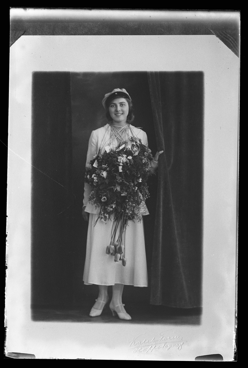 Porträtt av en kvinna i vita kläder, studentmössa och med blommor om halsen. I fotografens anteckningar står det "Rep.[ro] för Hans Gustafsson".