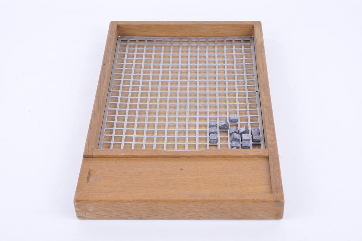 Rektangulært brett av tre. Bunnen har en metallplate med kvadratiske hull i. 132 kvadratiske metallterninger med punkt-tegn på, som kan plasseres i metallplaten. Brettet har en skuff på den ene kortsiden, der brikkene kan oppbevares.