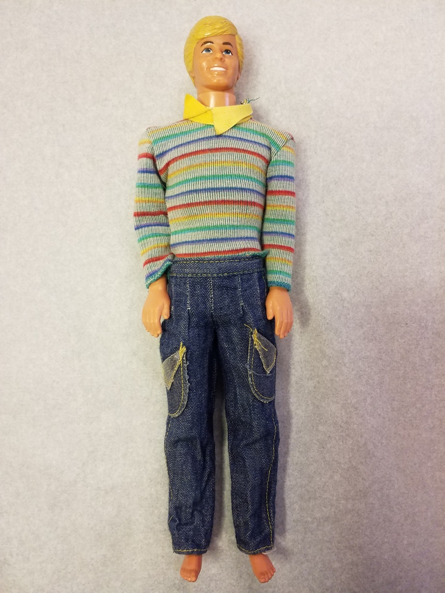 Mannedukke med kort blondt hår, stripete genser, jeans og grå sko.