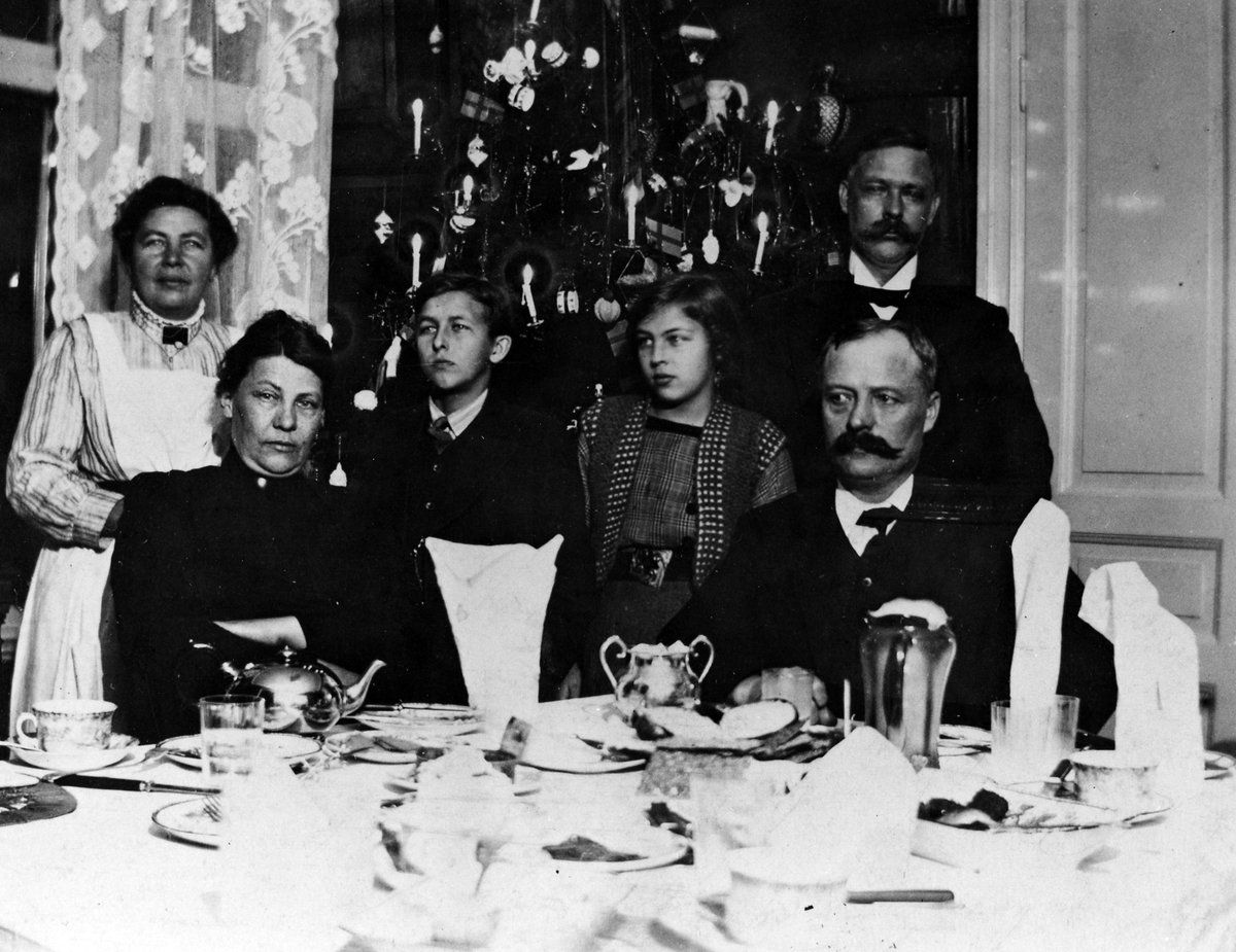En familj poserar för kameran vi juletid, makarna Wessman sittandes och barn och tjänstefolk står bakom.

Hos familjen Wessman på Norra Strömgatan 34 i Alingsås.